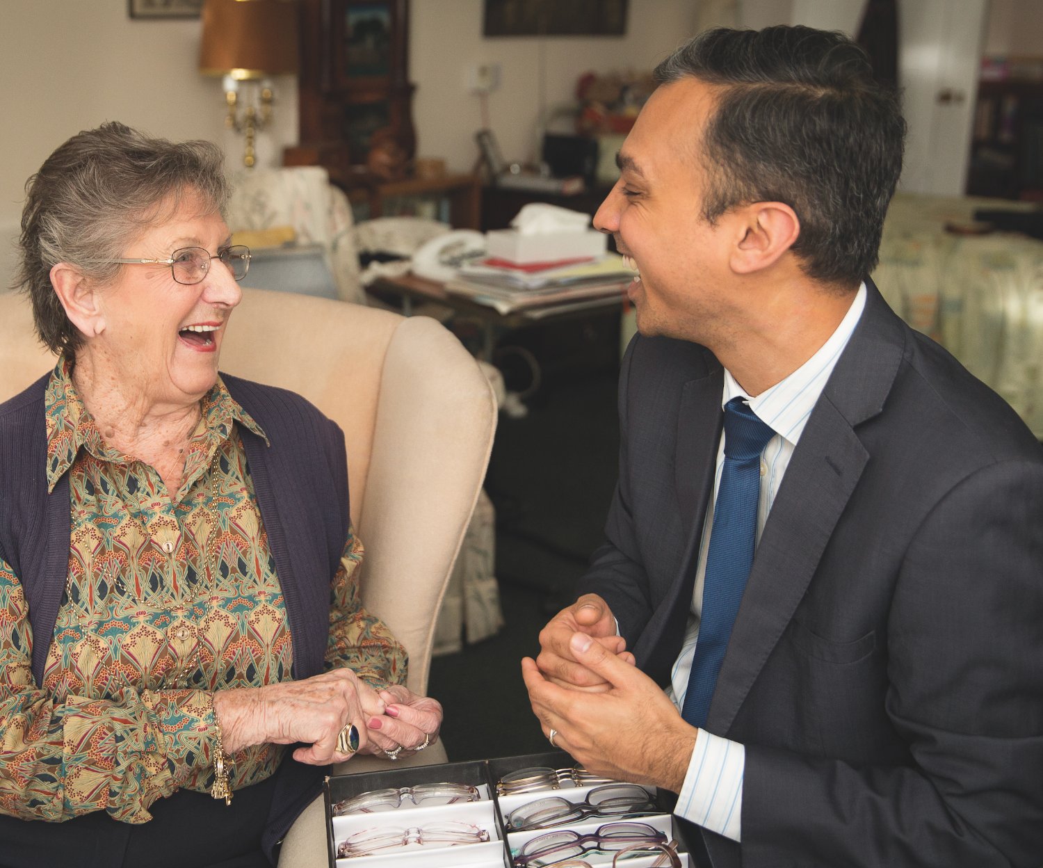 An Opticall optician laughing with an older resident as she chooses glasses from a frame case at home